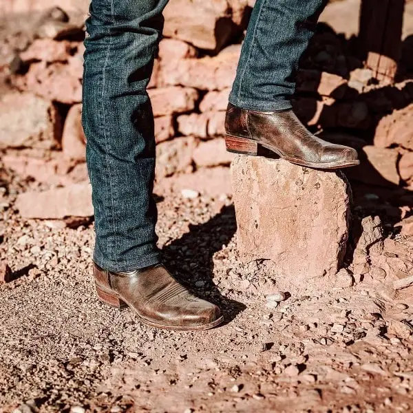 Man are standing on the rock with his jeans and cowboy boots