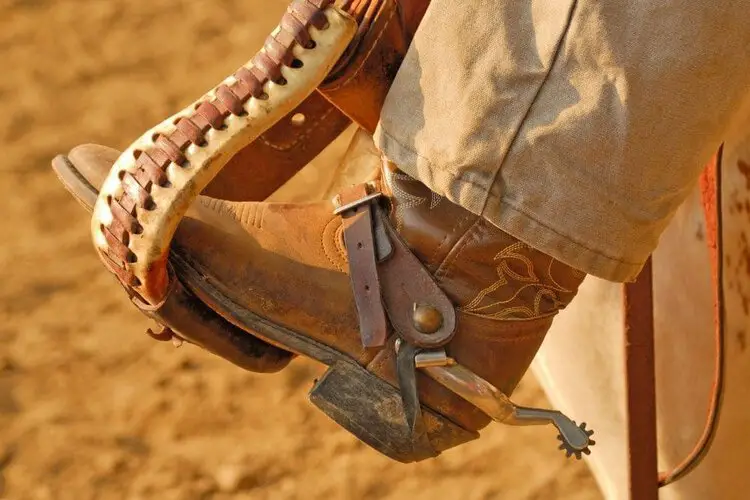 A man wear cowboy boots with khaki pants for riding a horse.