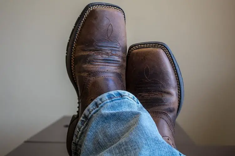 Man wear cowboy boots and put his leg on the table