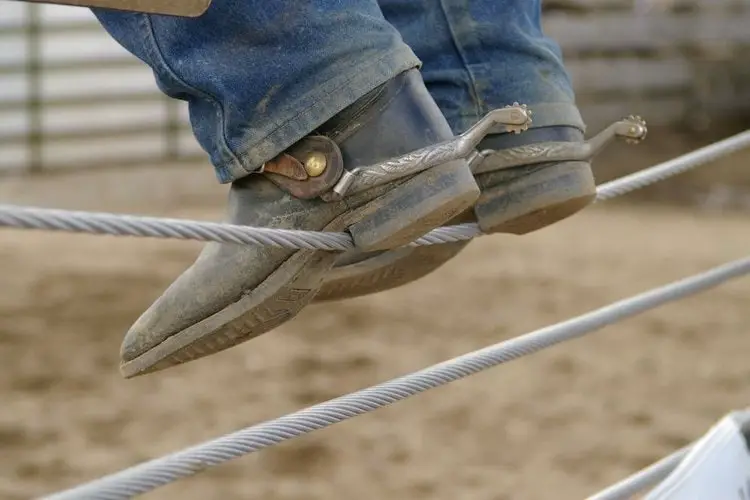 a man wears cowboy boots and sit on the fence