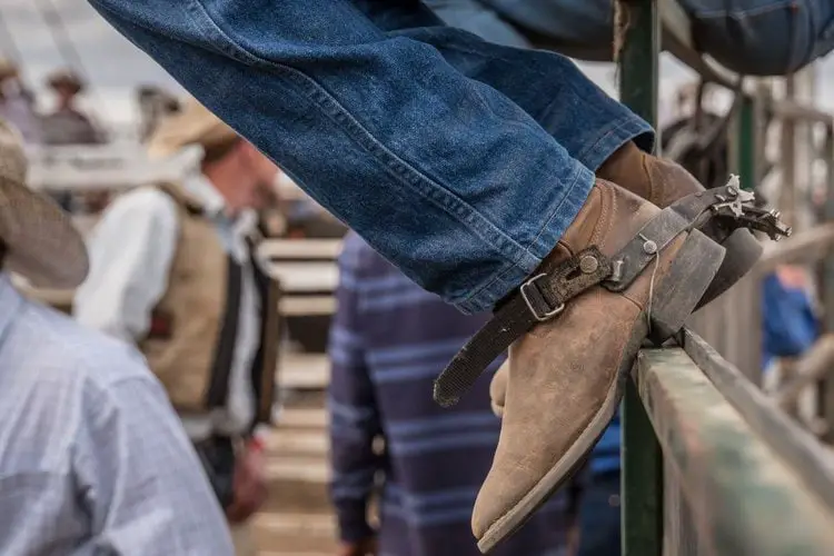 Man wear cowboy boots sit on the wooden fence