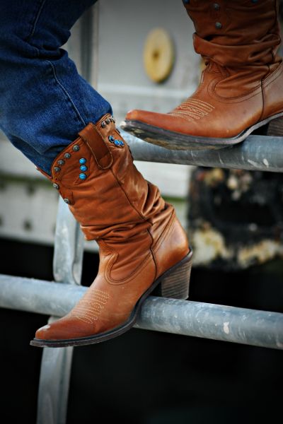 A girl wear cowboy boots and sit on the fence