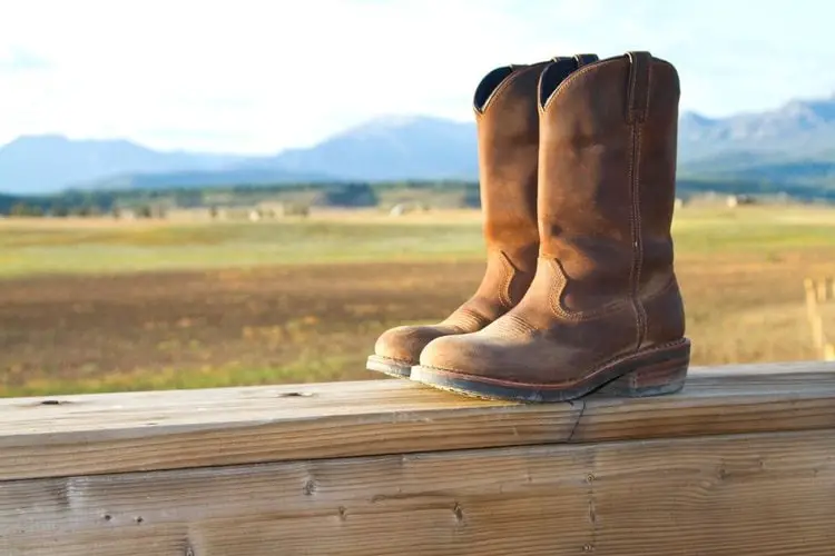 A pair of cowboy work boots on the wood fence