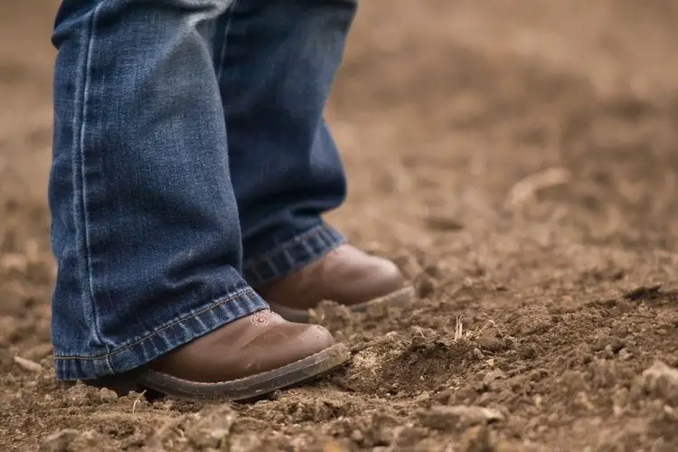 kid wear cowboy boots stand on the muddy ground