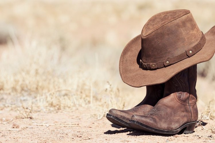 A pair of cowboy boots and cowboy hat under the sun