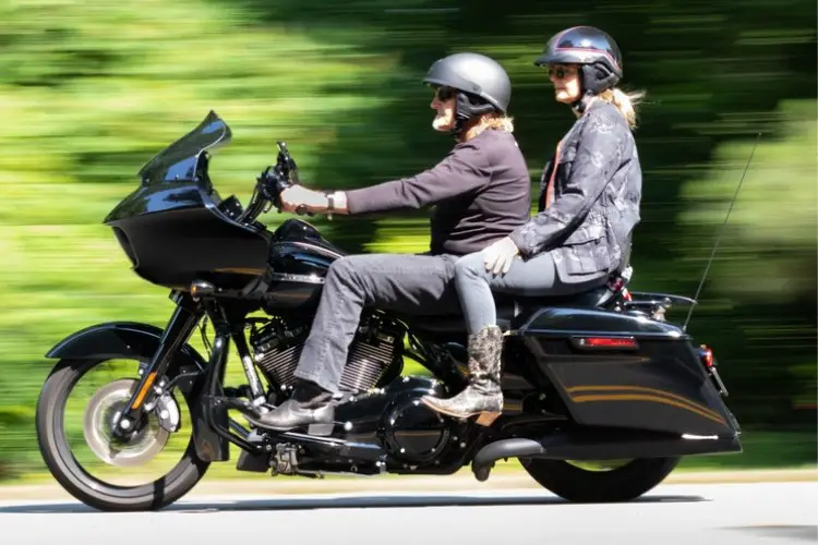 A man and a woman wear cowboy boots and are riding a motorcycle