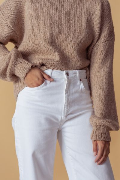 A woman wears brown sweater with white skinny pants