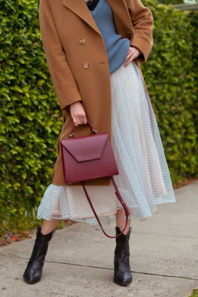 A woman wears cowboy boots with a skirts, sweater shirts, and a blazer