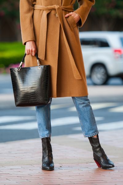 A woman wears jeans, cowboy boots, and trench coat in the city