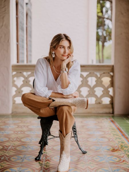 A woman wears the Jessie White ostrich cowboy boots and are sitting on the chair