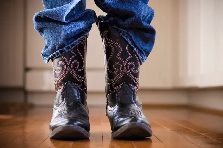 Man wear jeans and cowboy boots and are standing on the wooden floor