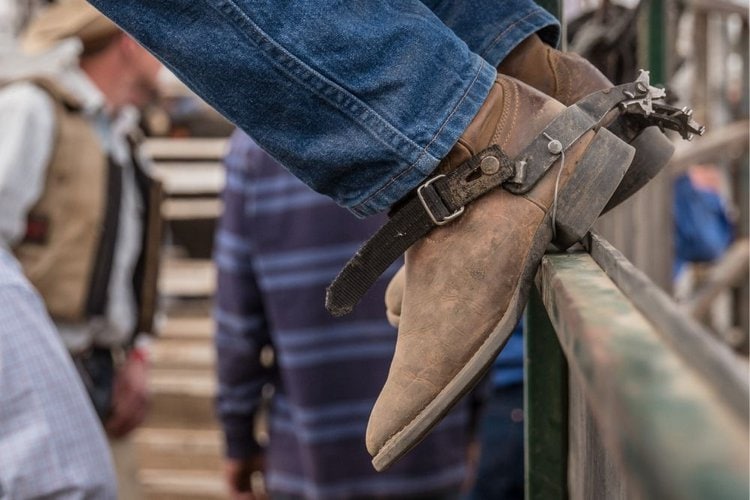 men wear cowboy boots with spur sit on the wood fence
