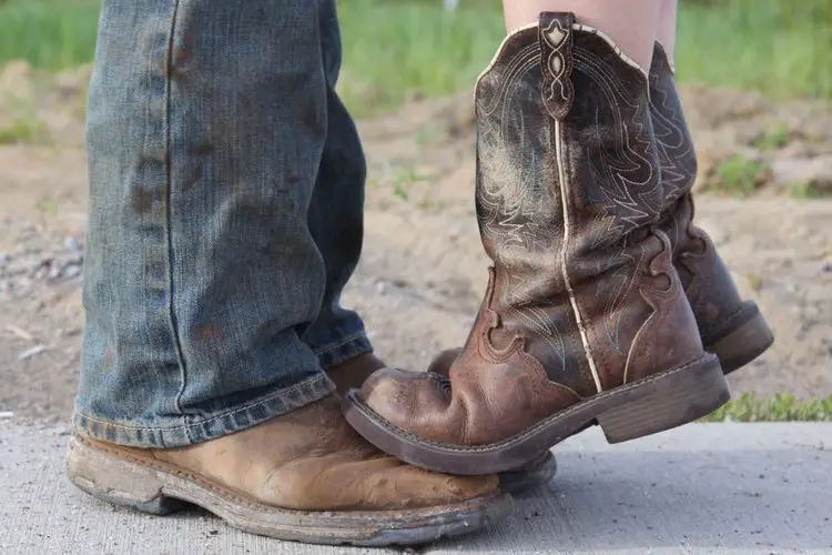 Women wearing cowboy boots stands on the feet of another man wearing cowboy boots