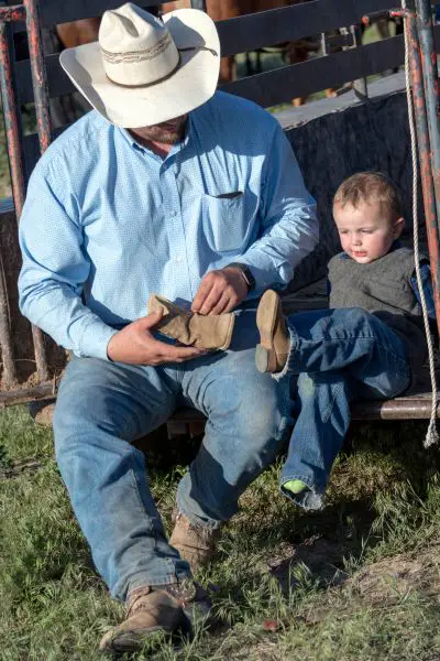 A cowboy dad wears cowboy boots for his toddler son
