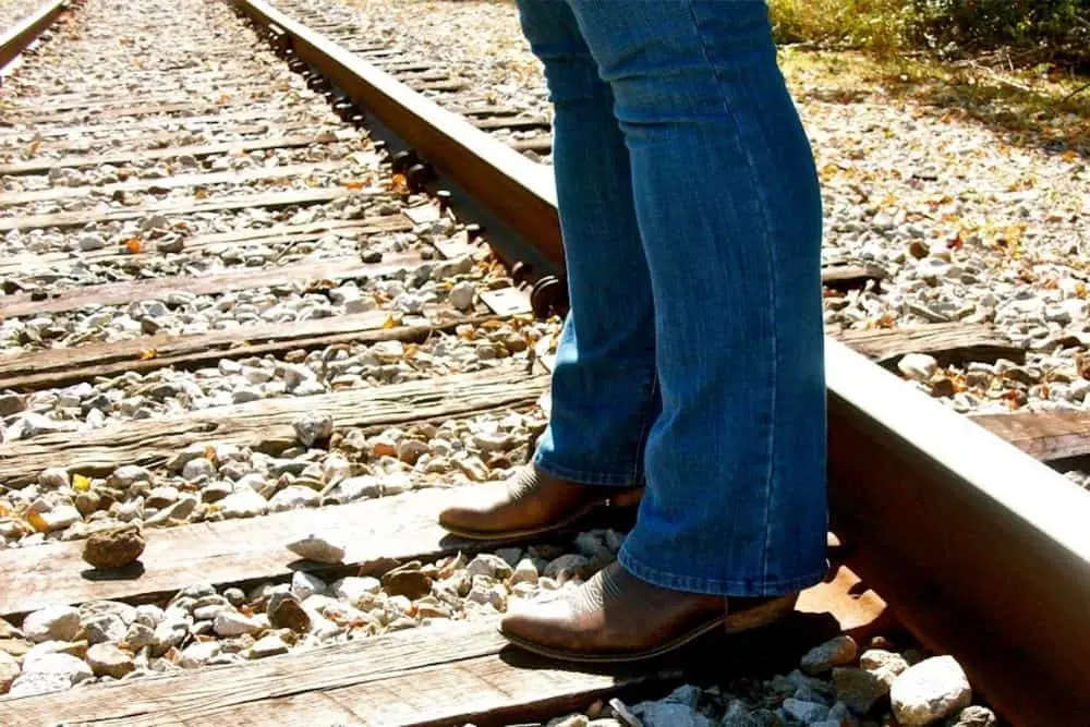 Woman in jeans and cowboy boots standing on train tracks