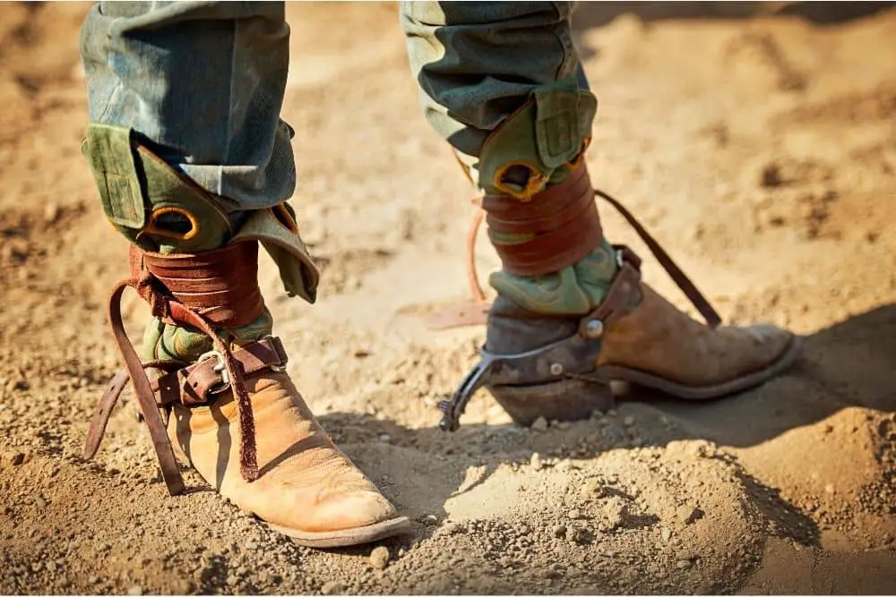 A man wears cowboy boots with leather strings wrap around the shaft