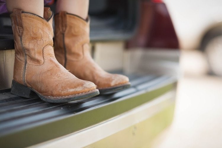 Girl wear cowboy boots and sit on back of the truck