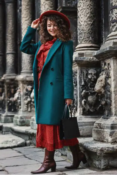 A woman wears long red dress, coat and cowboy boots