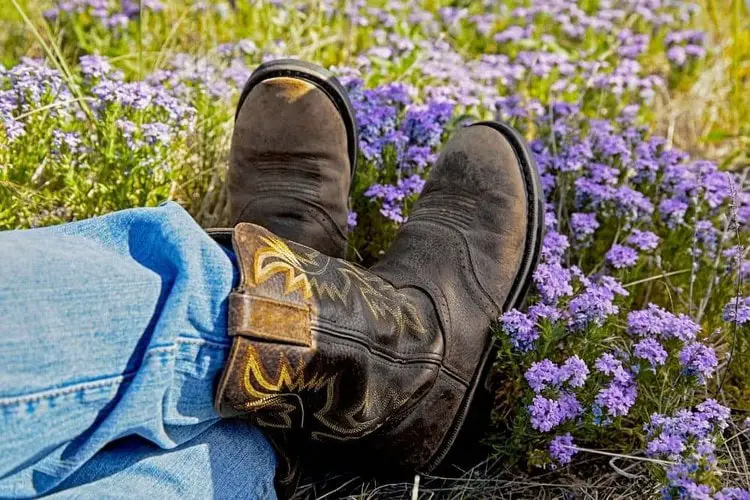 a person wearing jeans and cowboy boots sitting on flower field