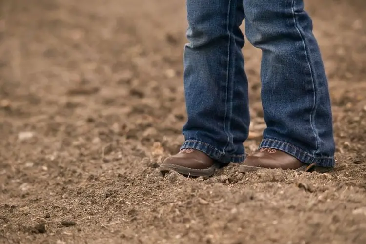 kid wear cowboy boots walking in the muddy ground