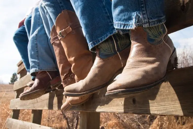 Men wear cowboy boots sit on the wooden fence