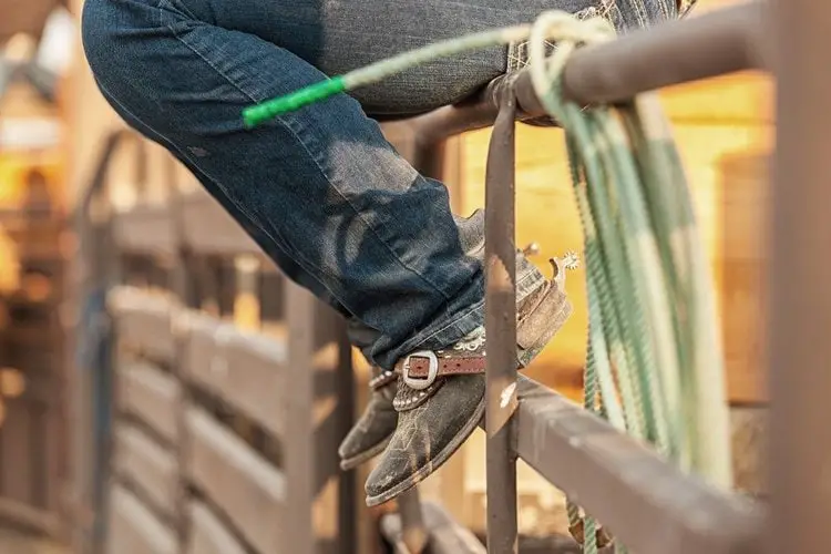 Men wear cowboy boots sit on the wooden fence