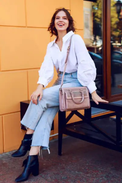 A woman wears jeans with blouse and black boots and handbag