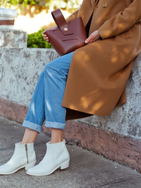 A woman wears white cowboy boots with ripped jeans and jacket