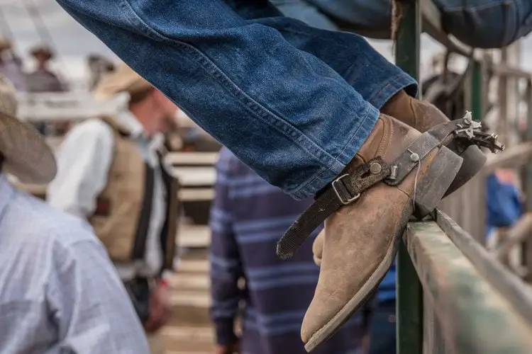 Man wear cowboy boots with straight jeans sit on the wooden fence