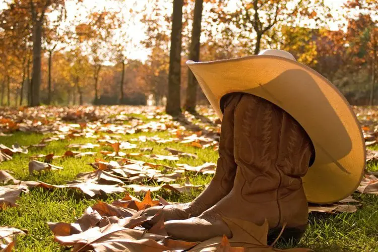 A pair of cowboy boots and cowboy hat on the ground under the sun