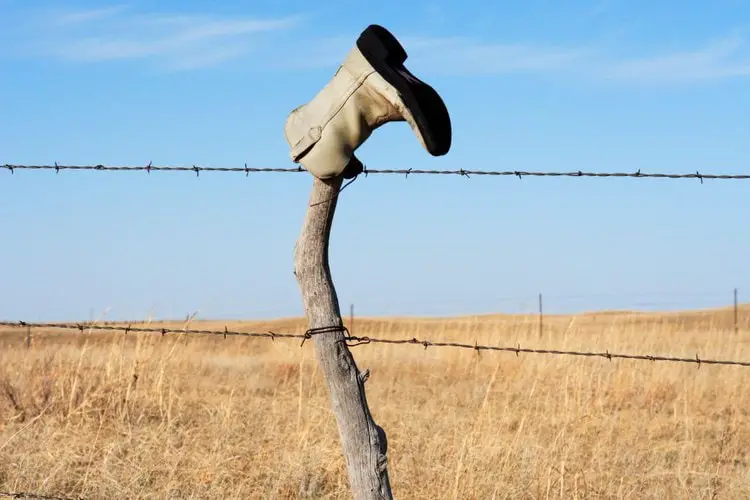 a cowboy boot is turned upside down to protect the top of a wooden fence post