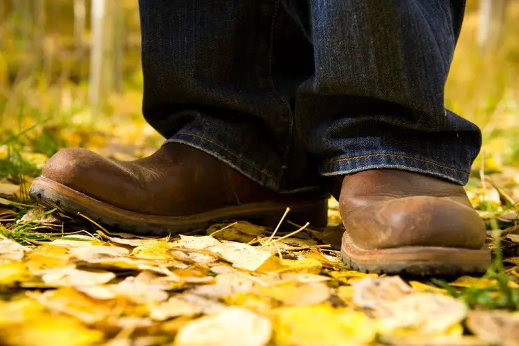 man wears cowboy boots and bootcut jeans standing yellow leaves