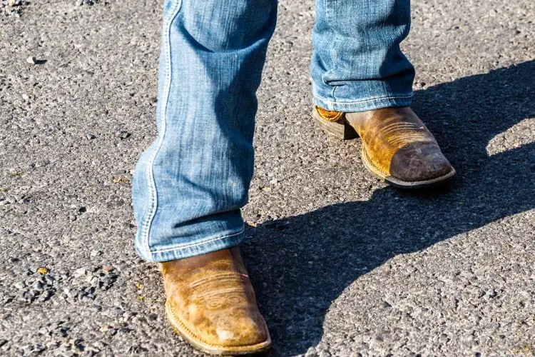 man wears cowboy boots and straight leg jeans standing on the road