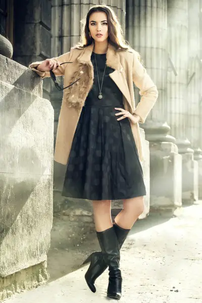 A woman wears black cowboy boots with black dress and tan blazer