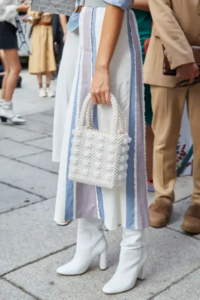 A woman wears neutral color dress with white cowboy boots and tote