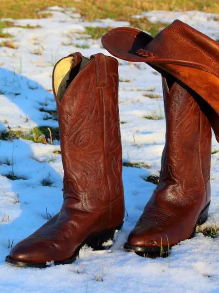 A pair of cowbot boots and a cowboy hat in the winter