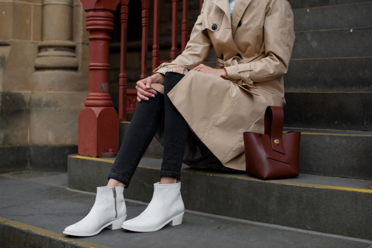 A woman wears black blazer with ripped jeans and white ankle cowboy boots