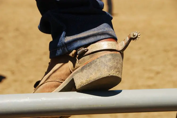 Man wear cowboy boots and are sitting on the fence