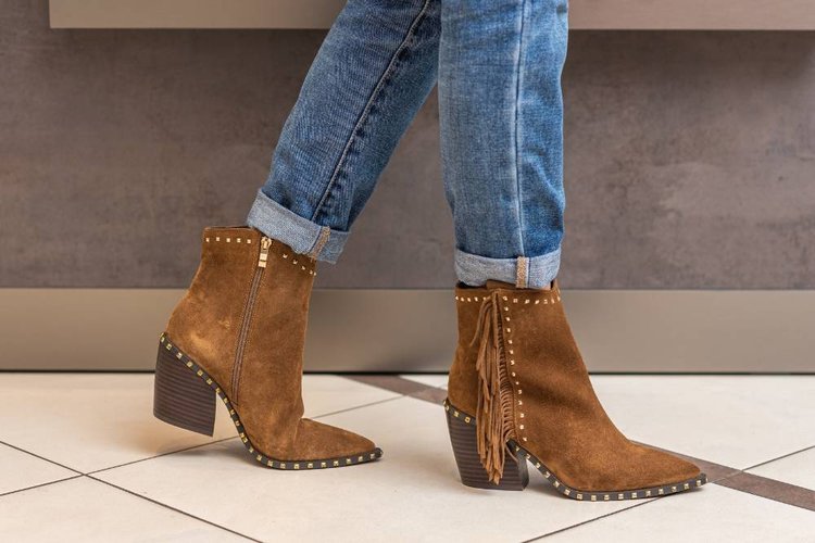 a woman cuffs her jeans to wear with suede boots