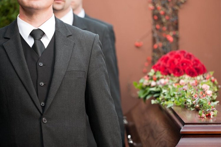 men wear suit in a funeral standing next to the coffin