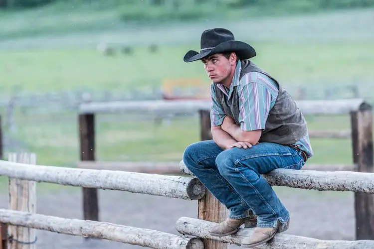 Cowboy sits on the fence with the jeans ripped in the hem.