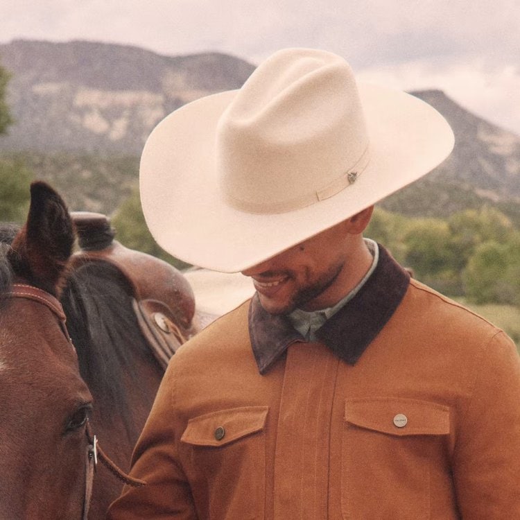 a man wears Tecovas cowboy hat standing next to a horse