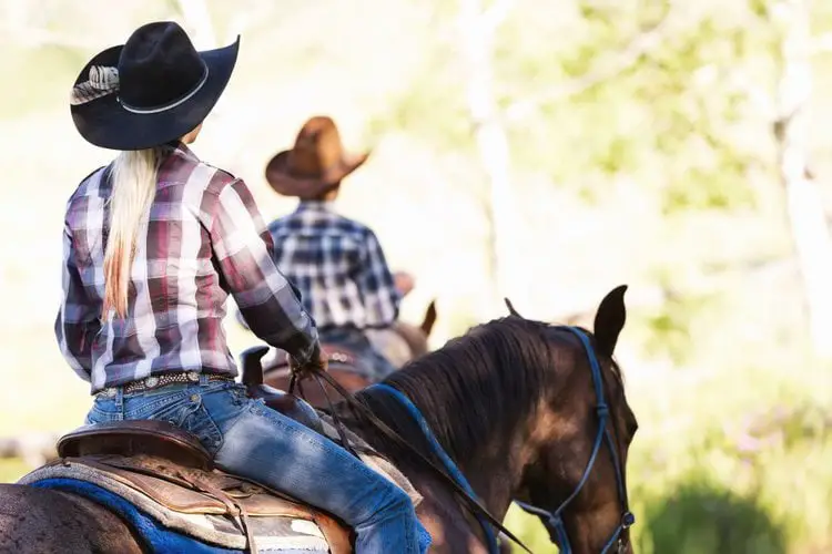 a woman riding a horse wears cowboy hat with a feather on the left