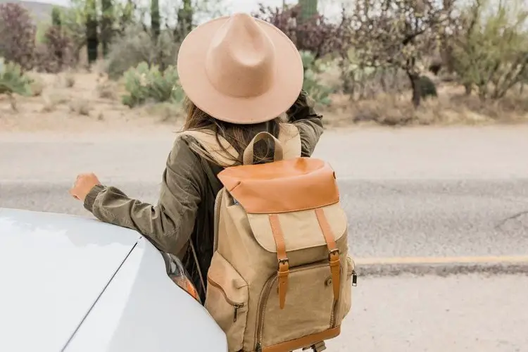 a woman wearing cowboy hat and backpack is going hiking