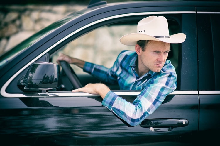 man wears cowboy hat in car checking the road