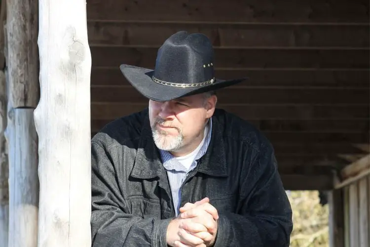 old man wears a black cowboy hat with holes on the side