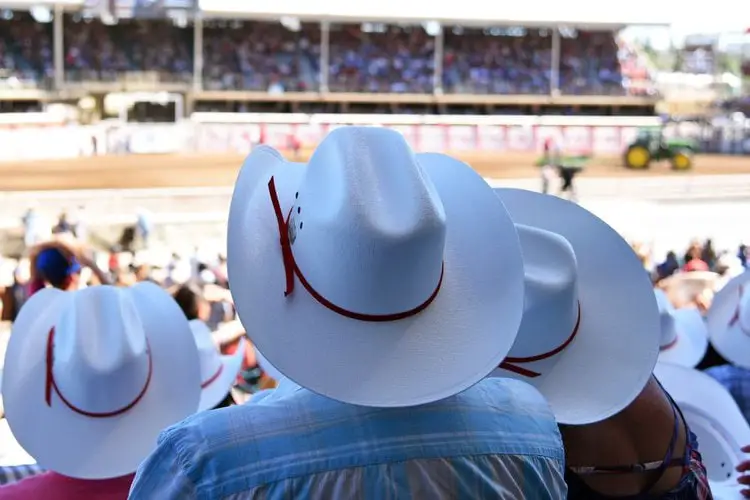people with curved up cowboy hats watching a monster truck racing league