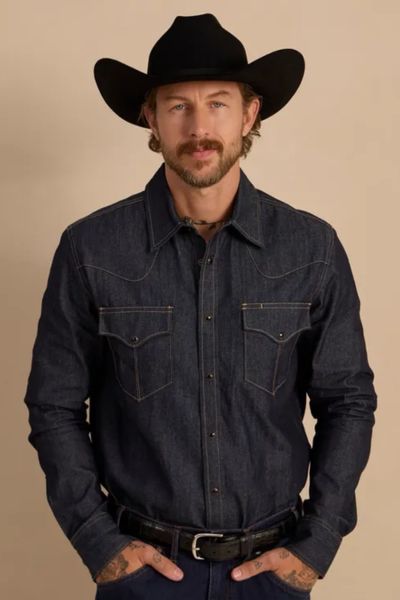 a man wears a dark wash denim pearl snap shirt