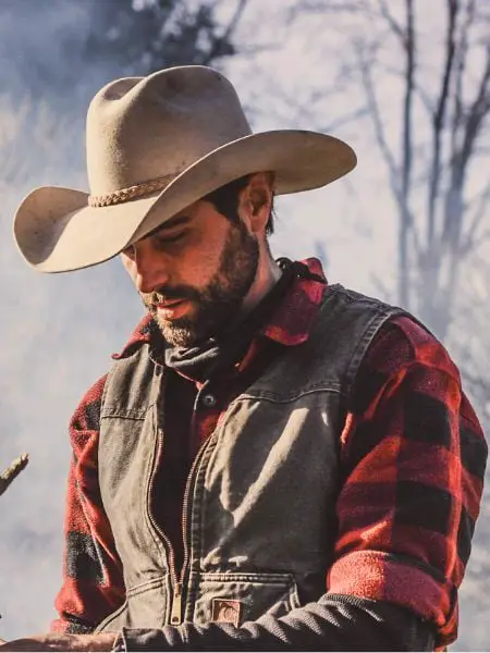 A cowboy wears vest with plaid shirt