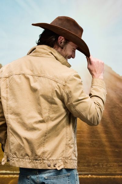 A man is using hand to hold a cowboy hat on the head